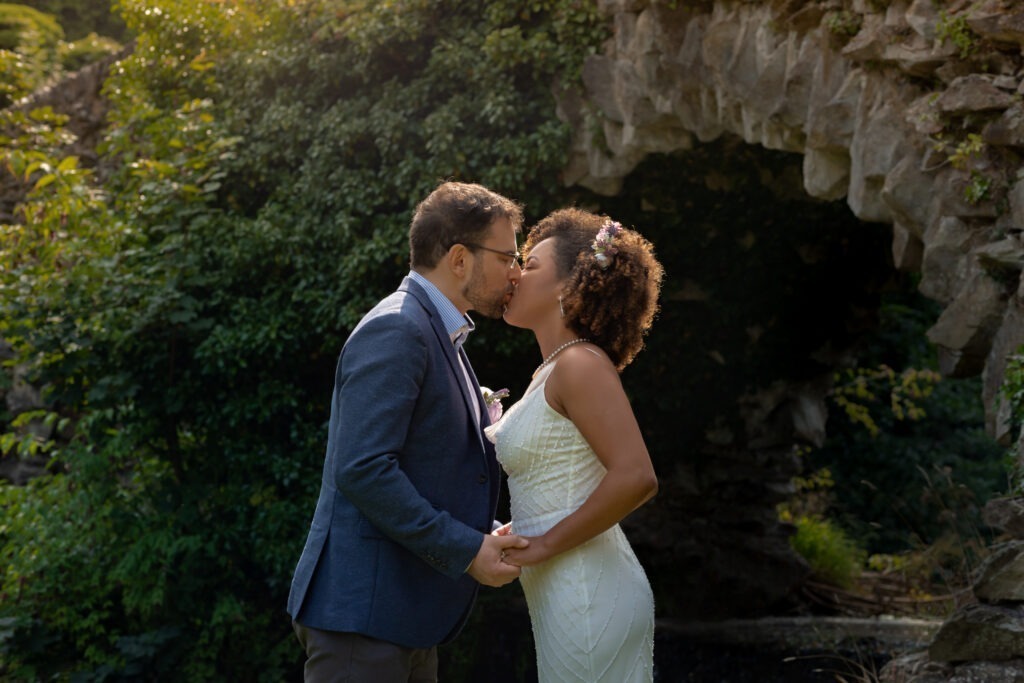 Bride and groom kissing beside a stone grotto in a garden
