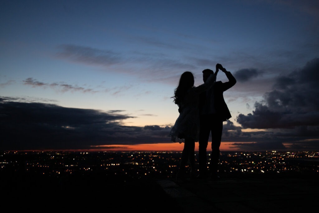 Silhouette of a bride and groom dancing at dusk above city lights