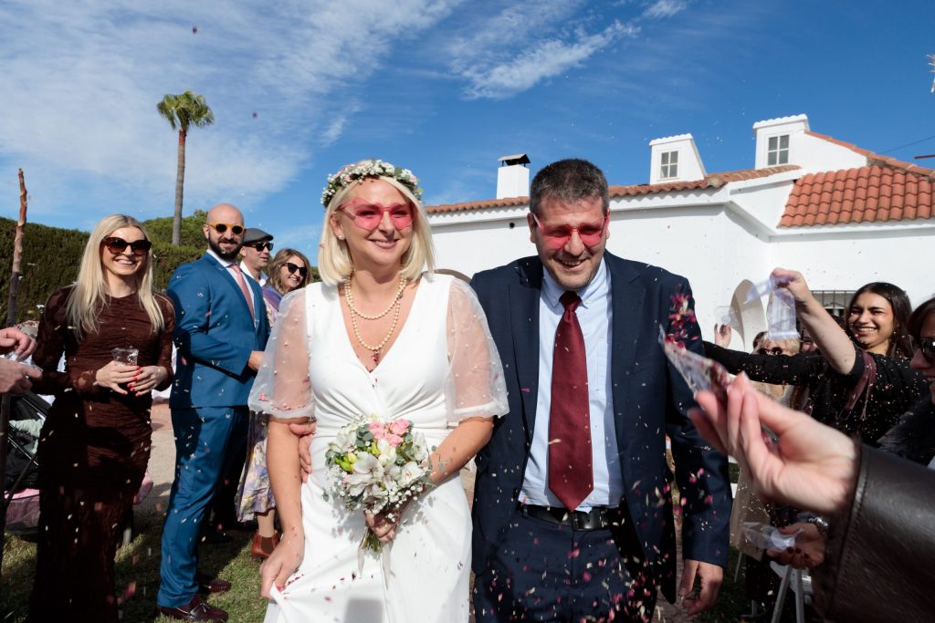 Bride and groom smiling as wedding guests throw confetti